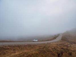 Morning mountain highway in dense fog. White car SUV with fog photo