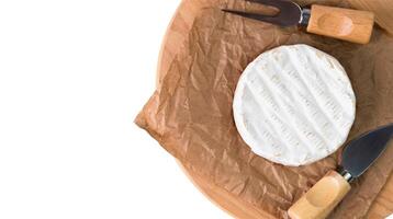 Camembert cheese and knives for cutting cheese on craft paper isolated on white background. Top view. Close-up. Selective focus. photo