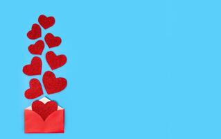 Red envelope and shiny red hearts on blue background. Congratulation concept. Flatlay. Top view. Copy space. photo