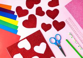 Red paper hearts, color papers, scissors, ruler, pen and pencil for Valentine's day card crafts on pink background. Top view. Flat lay. Step by step photo instruction. Step 3.