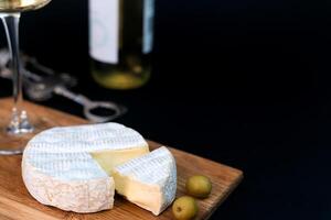 Camembert cheese, olives and wineglass of white wine on a dark background. Close-up. Copy space. Selective focus. photo