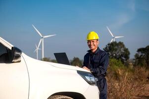 A wind turbine maintenance engineer is checking the operation of a wind turbine on a laptop placed on the hood of a pickup truck photo