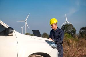 wind turbine maintenance engineer is checking the operation of a wind turbine on a laptop placed on the hood of a pickup truck photo