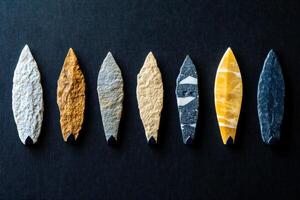 Collection of Native American arrowheads made of stone on dark fabric background with informative labels detailing each piece photo