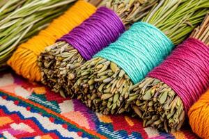 Close-up view of sage and cedar bundles wrapped in colorful threads on a vibrant Native American patterned cloth backdrop photo