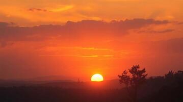 The sun sets over a hillside with trees in the foreground photo