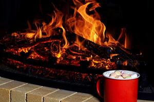 red mug filled with a warm, sweet Christmas drink topped with marshmallows stands out against the shimmering backdrop of a cozy fireplace photo