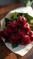 Elegant bouquet of rich red roses wrapped in delicate paper on wooden surface photo