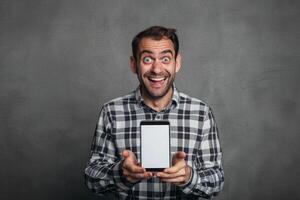 Excited man holding blank screen tablet against gray background photo