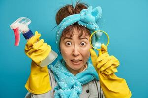 Surprised woman cleaning with spray bottle and magnifying glass in blue background photo