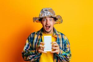 Surprised man in tinfoil hat holding tablet against bright yellow background photo