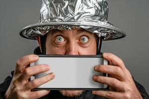 Man with tinfoil hat staring at smartphone in paranoia concept photo