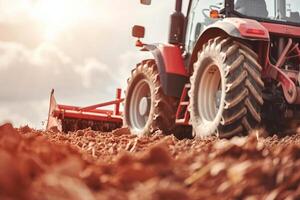 Red tractor plowing a field at sunset with close-up on soil and agriculture equipment photo