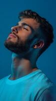 Young man expressing tranquility with closed eyes against a serene blue background, capturing a moment of introspection photo