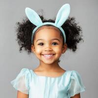Young girl with curly hair wearing bunny ears smiles brightly in a light blue outfit, capturing a joyful moment with innocence photo