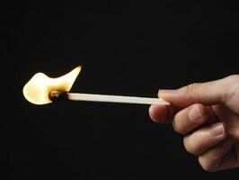 Hand holding a lit matchstick against a dark background capturing the moment of ignition and flame photo