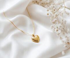 Elegant gold heart necklace resting on soft white fabric with delicate flowers in the background photo