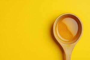Wooden spoon filled with liquid honey on a bright yellow background, emphasizing the sweetness and natural quality of honey photo