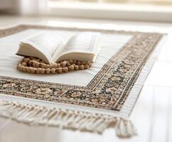 Open Quran resting on a prayer mat surrounded by prayer beads in a serene indoor space photo