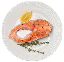 Raw piece of trout in white round plate and lemon slice, isolated background. photo