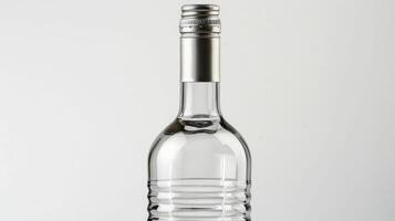 A clear glass bottle with a silver cap and ridges stands upright on a white surface photo