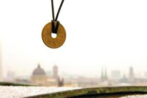 Lucky japanese 5 yen coin necklace displayed with a blurred foggy Berlin skyline in the background, symbolizing good fortune and cultural heritage. Selective focus. Copy space 2 photo