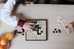 Close-up and top-view shots of GO, oriental checkers board game on wooden table are played by two Asian players, leisure time hobby, strategy decision and tactic challenge with compete concentrate. photo