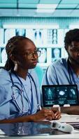 Vertical Healthcare professionals discussing patient health records during a meeting, utilizing modern diagnostic tools and technology in a well equipped doctor office. Assistants work with medic. Camera B. video