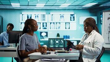 Black medic practitioner takes blood pressure with a blood pressure monitor, does a consultation with female patient using modern advanced tools for the checkup routine. Camera B. video
