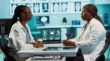 Black medical staff and patient discussing diagnostic feedback and records, emphasizing expertise and data driven decision making. Young adult listens to professional advice for wellness. Camera A. video
