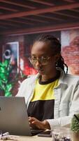 Vertical Portrait of smiling student at home browsing internet on notebook, doing homework, researching information online. Cheerful girl in apartment reading articles on laptop for school tasks, camera A video