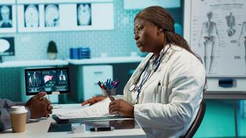 General practitioner reviewing x ray imaging at checkup with male patient, offering her professional expertise to ensure wellness. Medic doing scan interpretation with a man in the office. Camera A. video
