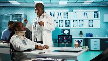 Black physician consulting her patient with injury by using stethoscope, listening to the lungs and heartbeat. Wheelchair user with a cervical foam at routine respiratory checkup. Camera B. video