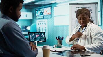 Female professional engaging in a conversation with a male patient, combining diagnostic technology and medical advice. Medic interacting with young man for health improvement. Camera B. video