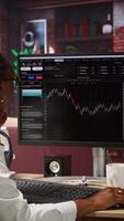Vertical Day trader using PC, purchasing stocks that might perform well and selling ones that might drop in value. Forex trader browsing though stock exchange portfolio pages at computer desk, camera A video