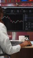 Vertical Day trader using PC to purchase and sell stocks, browsing through documentation files to learn how to maximize profits. Investor looking at stock exchange graphs on computer monitor, camera B video