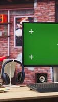 Vertical Green screen mockup desktop PC display on cozy home office desk with audio devices. Chroma key computer monitor in colorful modern loft with brick walls and plants on shelves video