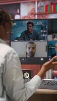 Vertical Remote worker in home office saluting coworkers during internet videocall, looking at PC monitor. Teleworker in apartment workspace waving hand, greeting team members during teleconference, camera B video