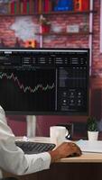 Vertical Day trader using PC, purchasing stocks that might perform well and selling ones that might drop in value. Forex trader browsing though stock exchange portfolio pages at computer desk, camera B video