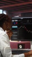 Vertical Day trader using PC to purchase and sell stocks, browsing through documentation files to learn how to maximize profits. Investor looking at stock exchange graphs on computer monitor, camera A video