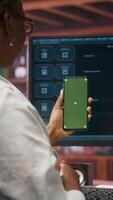 Vertical Woman uses green screen phone, doing videocall in front of PC screen with AI LLM chatbot answering prompt. Person uses large language model program during teleconference on mockup smartphone, camera B video