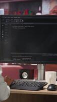 Vertical IT technician in home office looking at UI on computer monitor, executing programming script. Remote employee using coding application to write and test code in modern apartment, camera B video