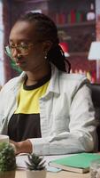 Vertical Teleworker drinking coffee while using notebook at home to write emails. Remote employee enjoying hot beverage and using laptop, composing documents to deliver finalized project paperwork, camera A video