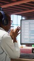 Vertical Excited programmer wearing headphones testing code on PC, clapping hands after seeing positive result. Upbeat woman at home overjoyed after fixing errors in application, listening music, camera A video