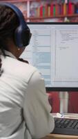 Vertical Excited programmer wearing headphones testing code on PC, clapping hands after seeing positive result. Upbeat woman at home overjoyed after fixing errors in application, listening music, camera B video