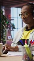 Vertical Teleworker listening music while typing on notebook keyboard in home office, writing emails. Remote employee wearing headphones using laptop, finishing project tasks, camera A video