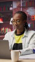 Vertical Bookkeeper in home office studying financial statements on laptop and writing down info. Teleworker in apartment reading documents on notebook and taking notes with pen on paper, camera B video