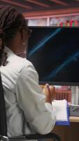 Vertical Student doing academic research on internet to gain financial knowledge useful for career development, taking notes. African american woman in online class doing courses, writing down info, camera B video