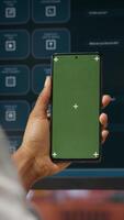 Vertical Woman using isolated screen smartphone and AI LLM chatbot on computer screen in home office. Person holding chroma key phone uses artificial intelligence chatbot on monitor, camera B video