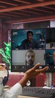 Vertical Remote worker in home office saluting coworkers during internet videocall, looking at PC monitor. Teleworker in apartment workspace waving hand, greeting team members during teleconference, camera A video